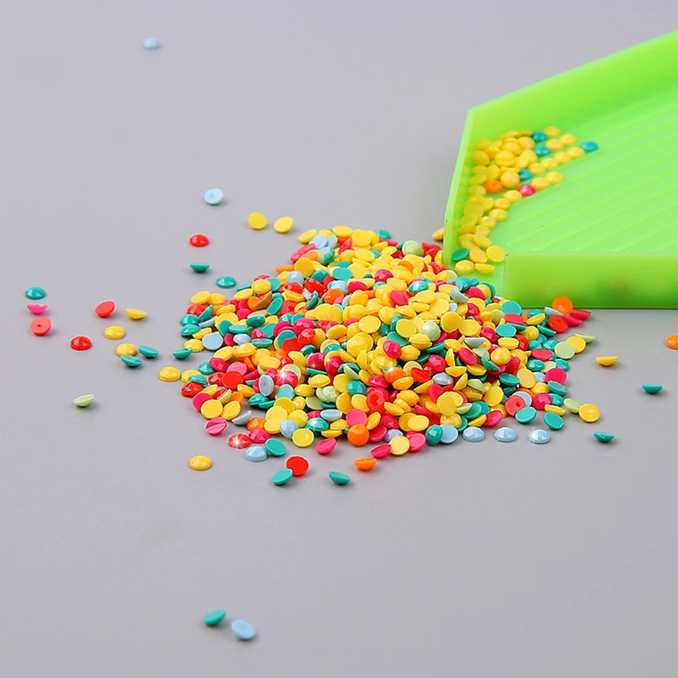 A pile of colorful sequins and small beads spills onto a gray surface next to a green tray.