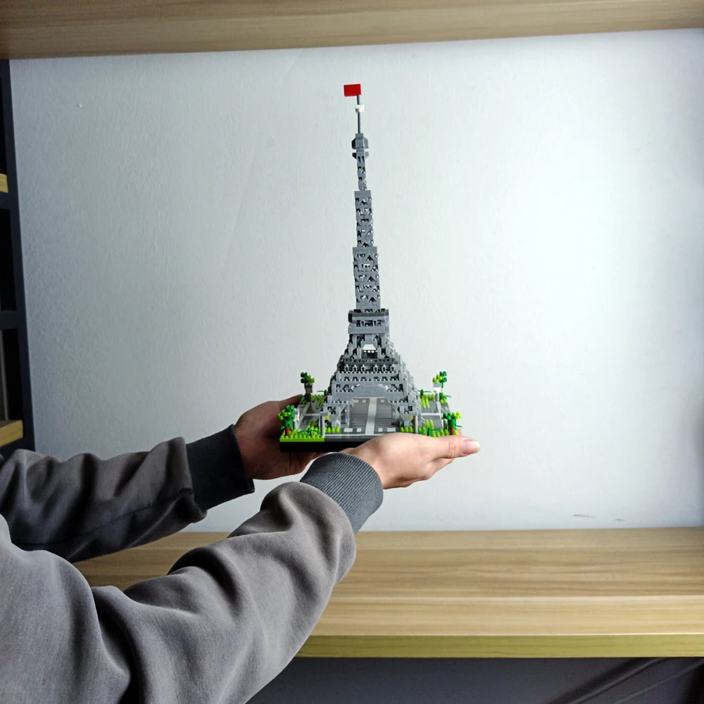 A hand holds a miniature model of the Eiffel Tower built from green building blocks against a white background.