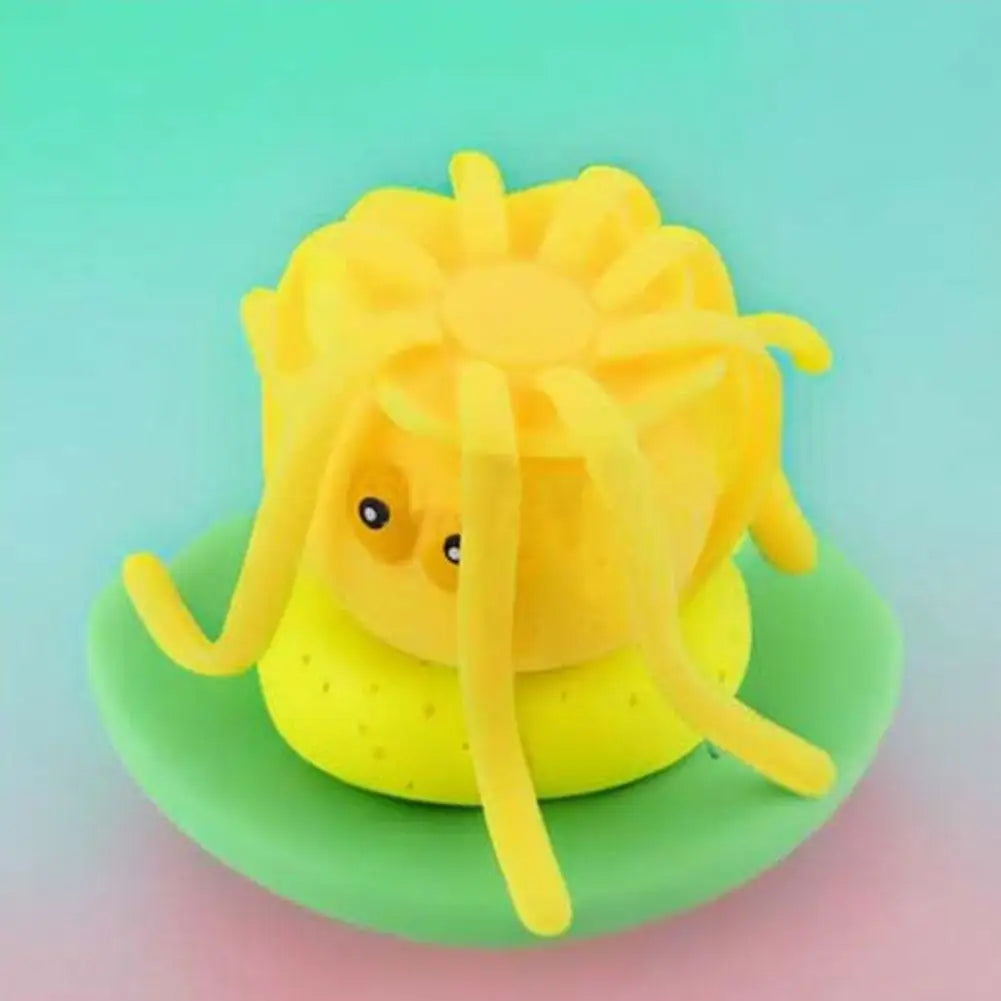A yellow silicone octopus bath toy is shown resting on a green surface.
