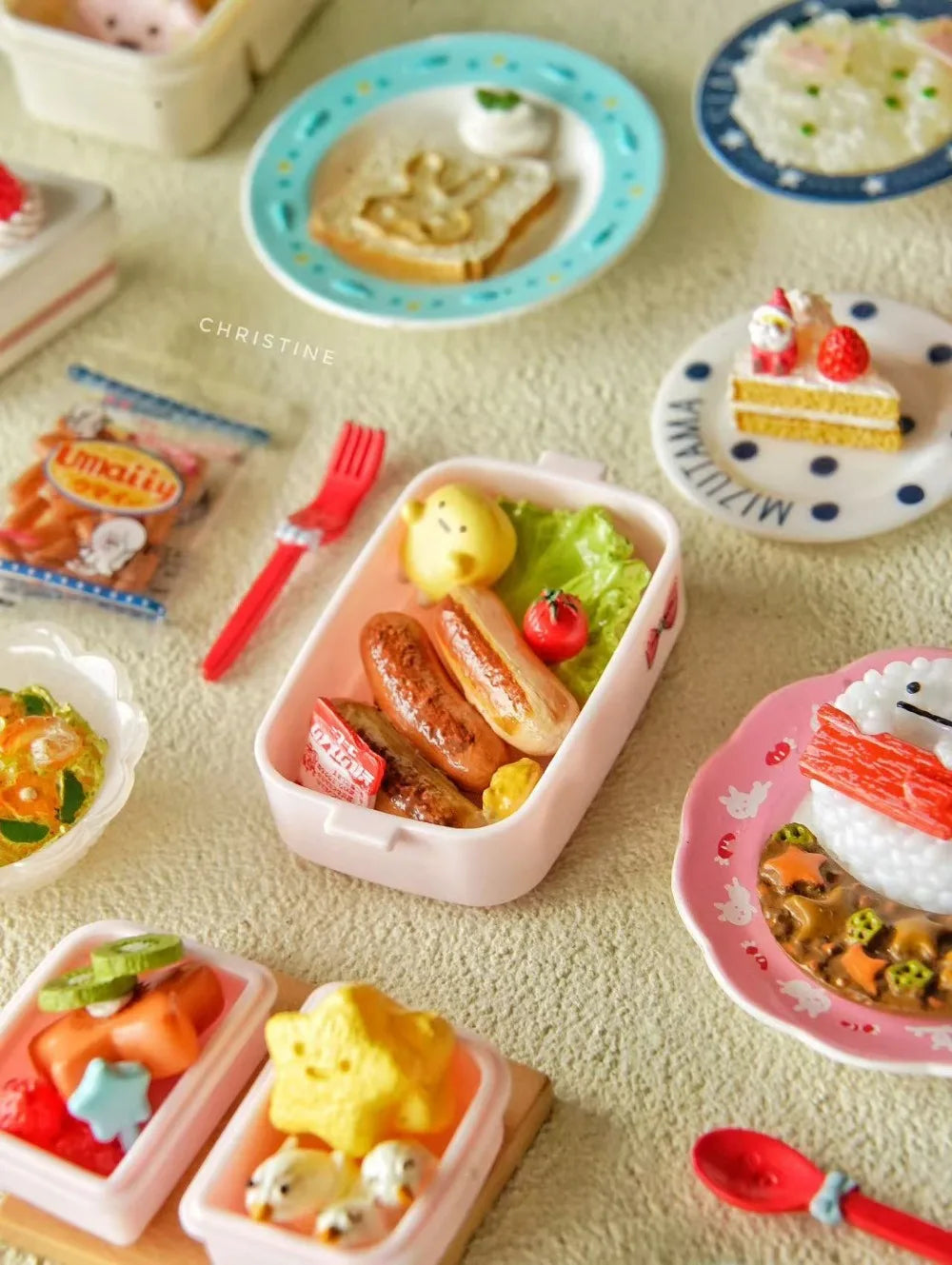 A collection of miniature food items and a doll picnic lunch box with a handle on a light surface.