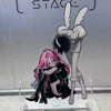 Acrylic figure of an anime character with pink hair and black clothing standing on a clear stand.