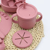 A pink 9-piece silicone baby tableware set with suction cups resting on a woven mat.