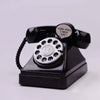 A vintage rotary telephone piggy bank with a black body and silver dial, featuring a circular emblem and a tag that reads Gir