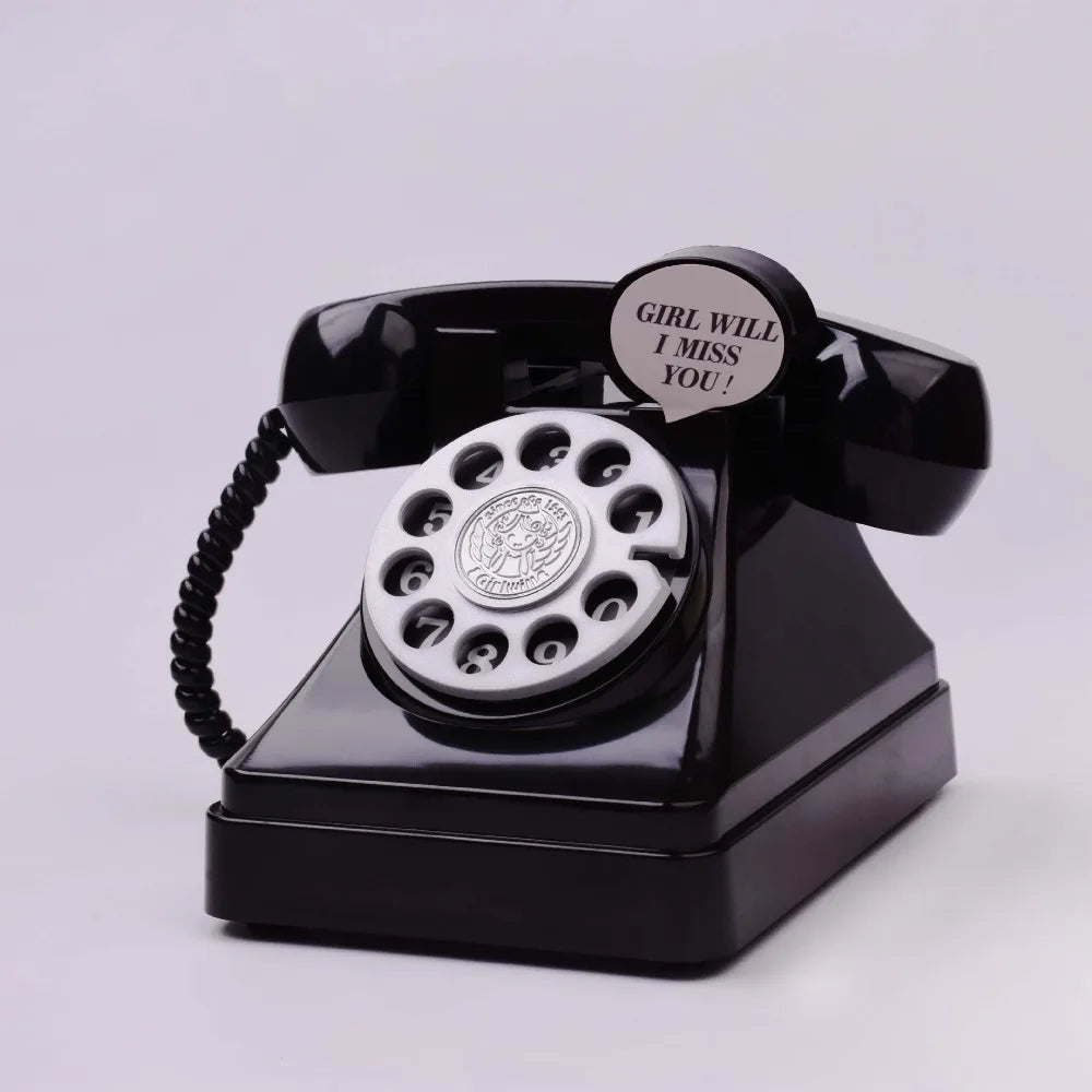 A vintage rotary telephone piggy bank with a black body and silver dial, featuring a circular emblem and a tag that reads Gir