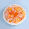 A mix of colorful, translucent acrylic beads in shades of orange, pink, and yellow is displayed on a white plate.