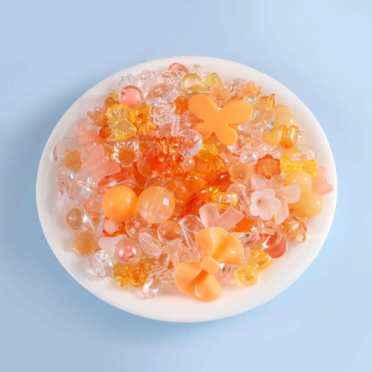 A mix of colorful, translucent acrylic beads in shades of orange, pink, and yellow is displayed on a white plate.