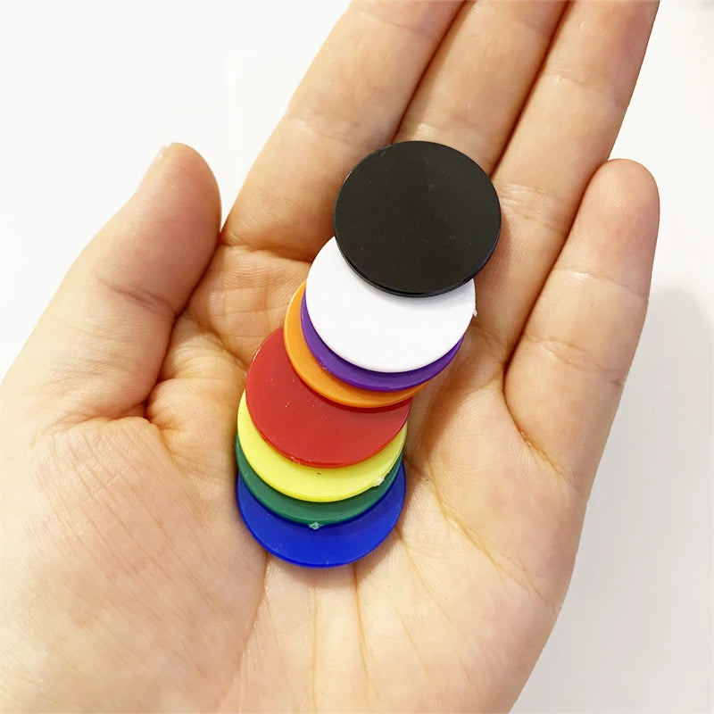 A hand holds a stack of colorful plastic game markers, ranging in color from red to black.