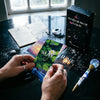 Hands hold a green oracle card from the Mystical Moon Oracle deck next to a dark box and a crystal rod on a black surface.