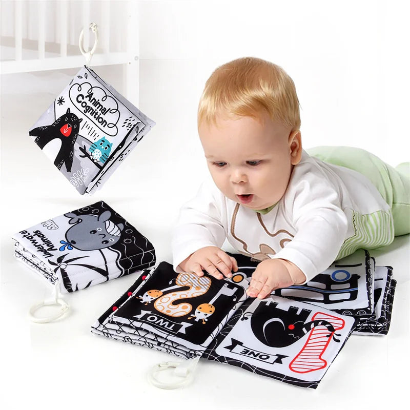 A baby is looking at a high-contrast soft cloth book featuring animals and cognition concepts.