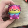 A small, squishy, colorful newt-shaped stress relief toy with a gradient of pink, yellow, and blue.