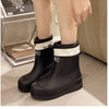 A pair of black waterproof mid-calf rain boots with white trim and a non-slip sole are shown on a floor.