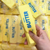 A hand holds a yellow butter stick squishy toy with the word BUTTER written on it.