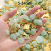 A hand holds a collection of light green imitation jade charms and gold jewelry components for crafting.