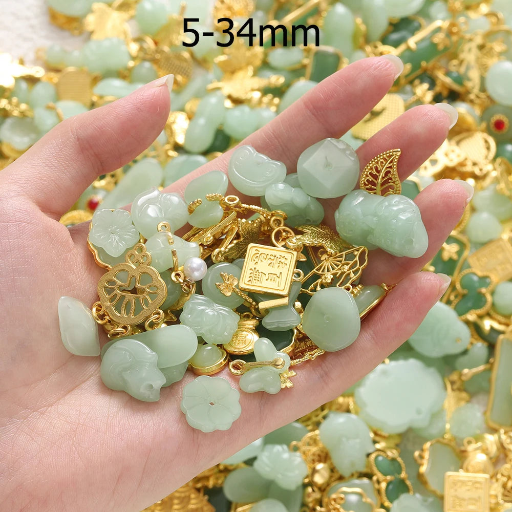 A hand holds a collection of light green imitation jade charms and gold jewelry components for crafting.