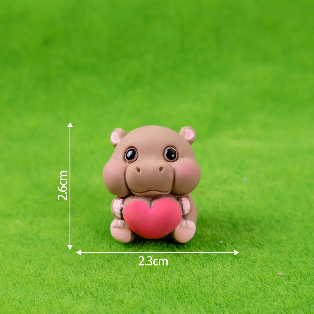 A small, pink resin hippo figurine with a heart detail is placed on green grass.