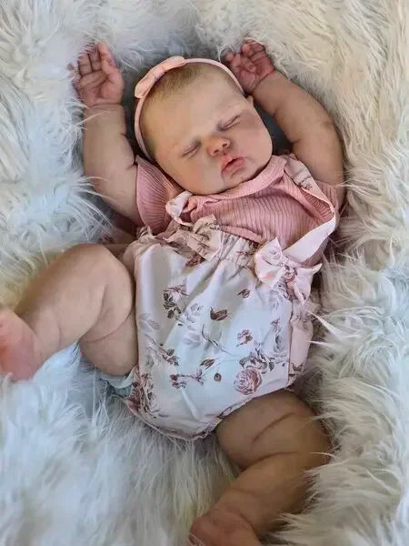 A newborn baby doll with hand-painted skin is sleeping on a fluffy white surface.