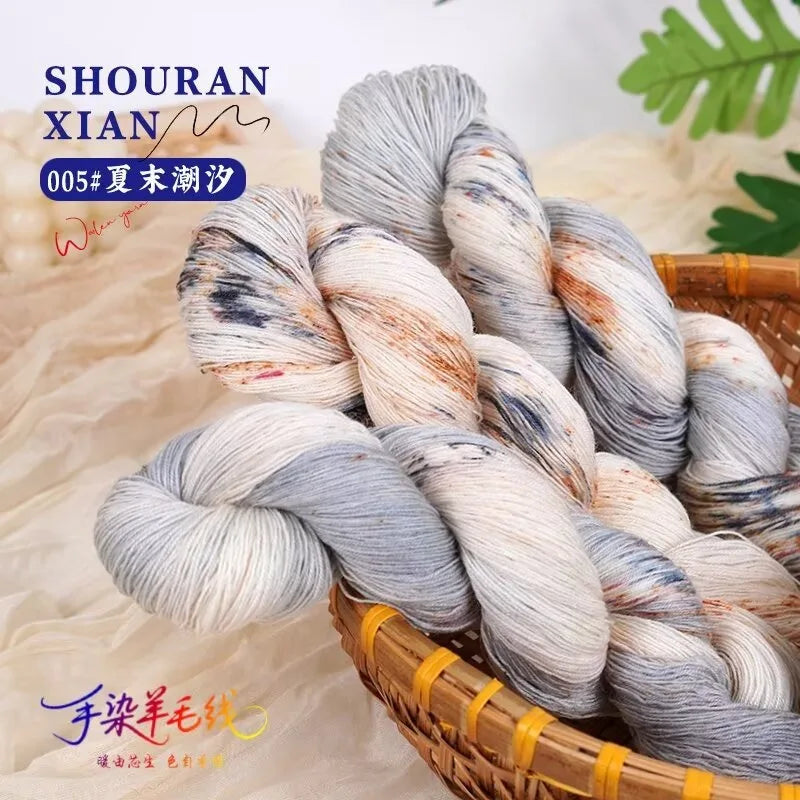 A bundle of hand-dyed Australian wool yarn showing a gradient of gray, white, and subtle brown tones, coiled in a wooden bask