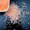 A pile of crushed pink and clear glass crystals scattered on a dark surface.