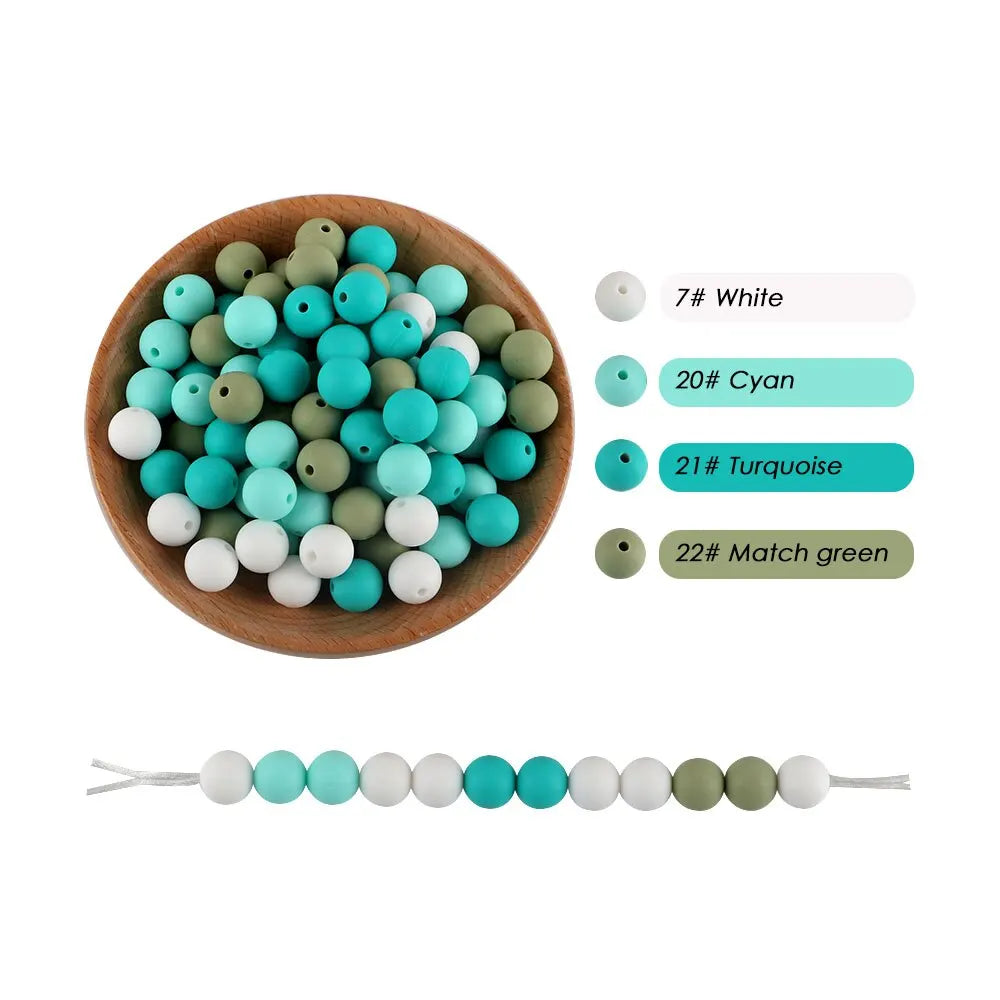 A collection of silicone round beads in white, cyan, turquoise, and matcha green colors displayed in a wooden bowl.