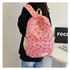 Un sac à dos rose avec un motif de nœud rouge porté par une personne sur fond blanc.