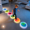 A young boy is walking across a floor marked with colorful LED balance stones, demonstrating an interactive learning mat for 