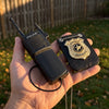 A hand holds a black walkie-talkie and a gold police officer badge accessory set.