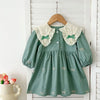 A sage green girls' party dress with white lace collar details hanging on a wooden hanger.