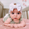A baby wearing a white bow headband, looking directly at the camera.