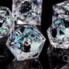 A close-up of a set of iridescent liquid core dice, including a hexagonal die and other polyhedral shapes, reflecting on a da