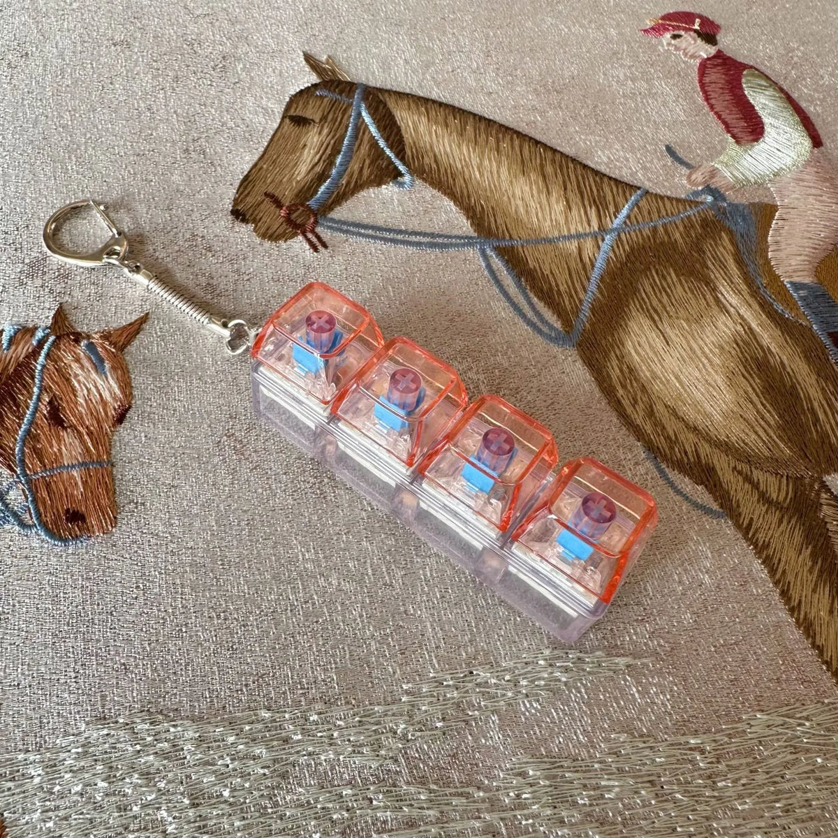A brown horse is shown next to a clear acrylic fidget keychain with four colorful key buttons.