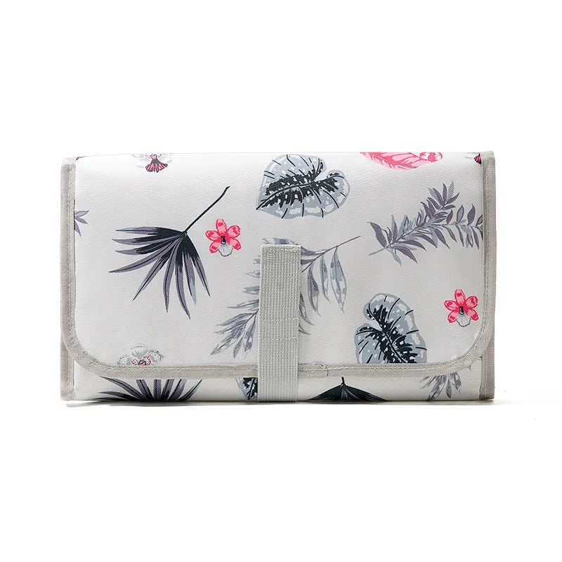 A white portable waterproof baby changing mat with a light gray carry handle and floral leaf pattern.