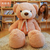 A large, light pink teddy bear plush toy sitting on a beige rug in front of wooden bookshelves.