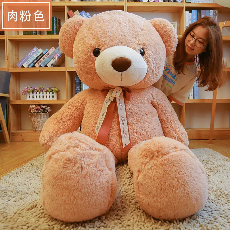 A large, light pink teddy bear plush toy sitting on a beige rug in front of wooden bookshelves.