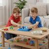 Two young boys play with a wooden four-in-a-row strategy board game on a light wood table.
