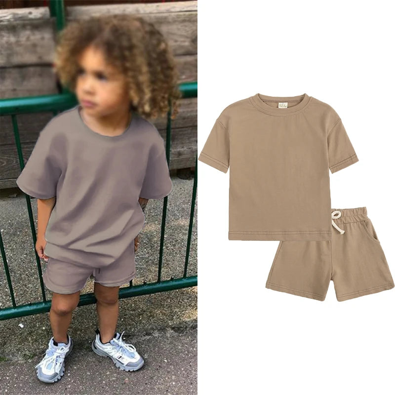 A child wearing a tan short sleeve top and matching shorts outdoors.