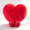 A bright red heart-shaped plush cushion with embroidered eyes and small pink feet.