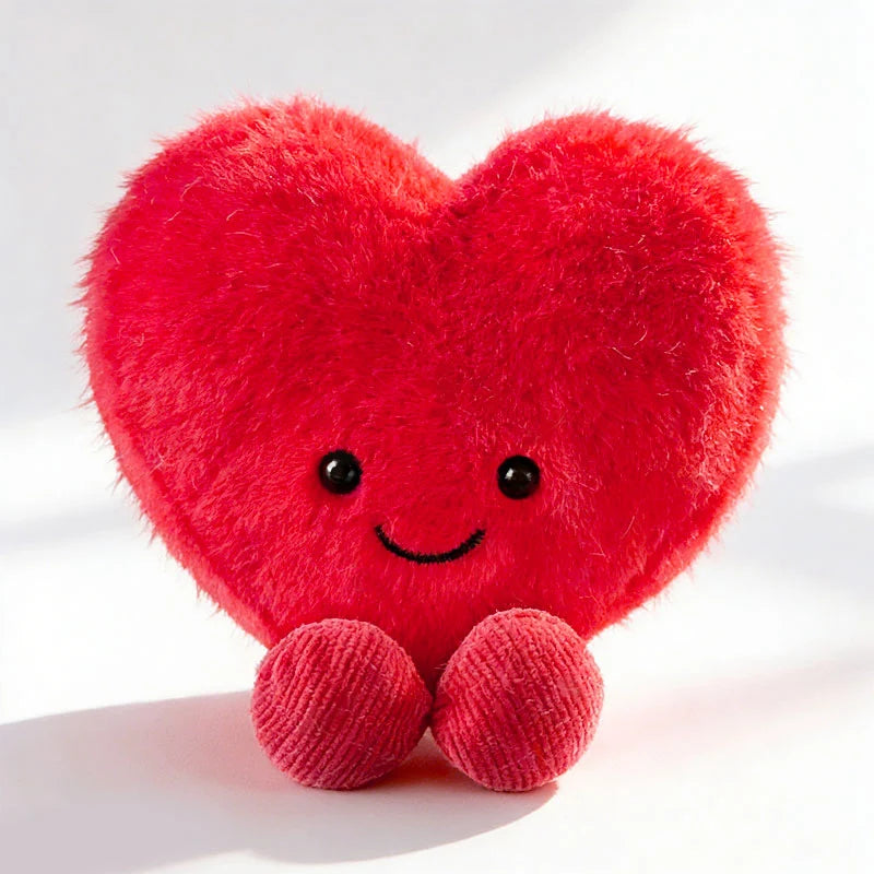 A bright red heart-shaped plush cushion with embroidered eyes and small pink feet.
