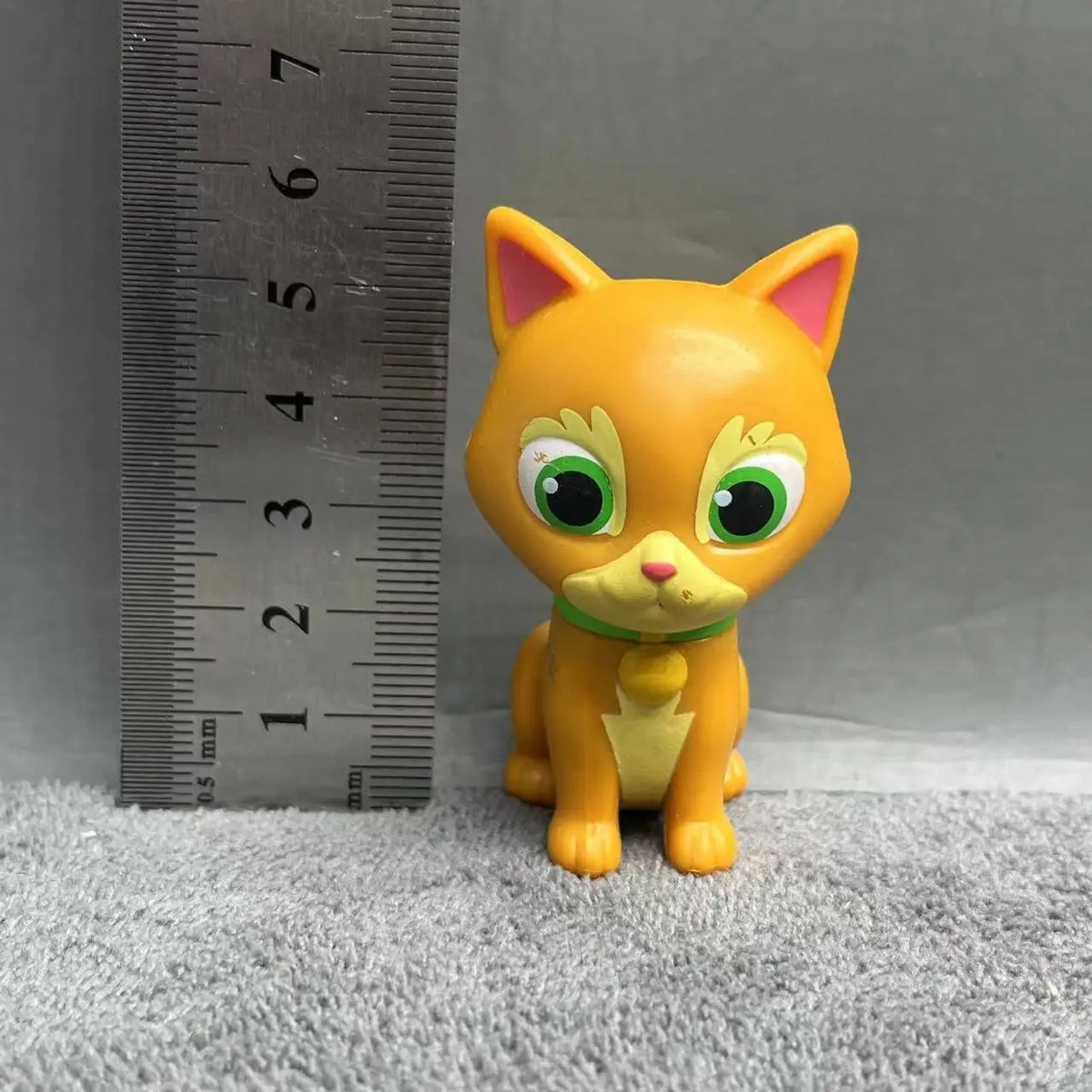 A yellow cartoon cat figurine with large green eyes and pink nose is shown next to a ruler.
