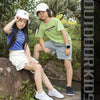 Two children sitting on a rock outdoors wearing casual clothing and white sneakers.