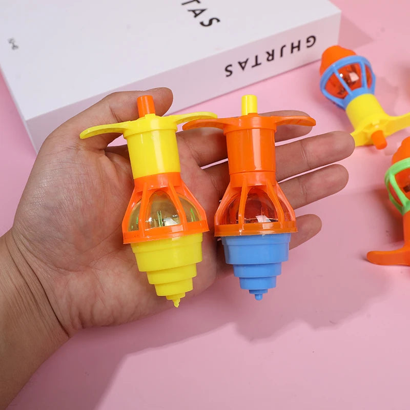 Two glow-in-the-dark spinning tops in yellow and orange are held in a hand against a pink background.