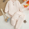 A light pink knitted baby romper and pants set laid on a white surface with natural fibers and autumn leaves.