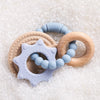 A set of food-grade silicone planet teethers in light blue and natural wood tones resting on white granular material.