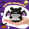 A handmade knitted black bat doll with purple wings and a gift card tag is shown in a hand against a purple background.