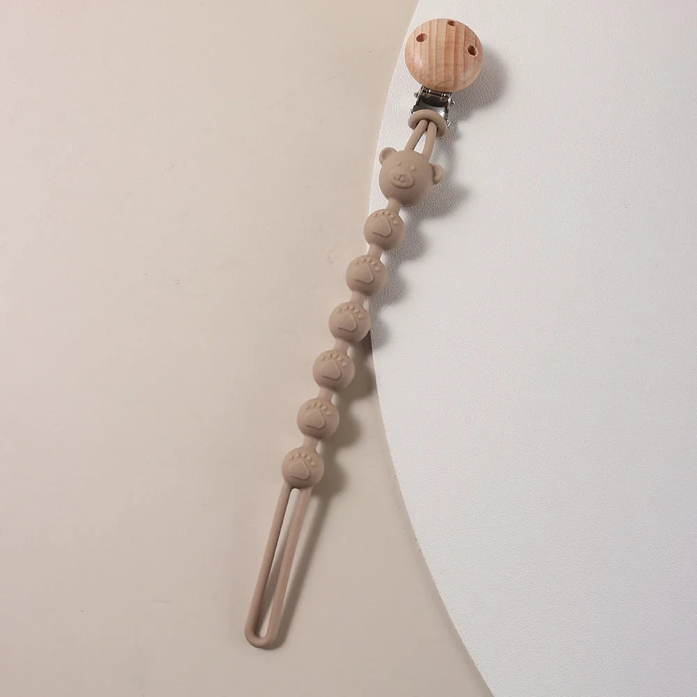A silicone bear paw pacifier clip with a wooden top and a flexible silicone chain.