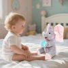 Un bébé est assis sur un lit avec un jouet d'éléphant en peluche à côté de lui.