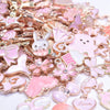 A close-up of a gold-tone enamel charm assortment featuring pink and white designs for jewelry making.
