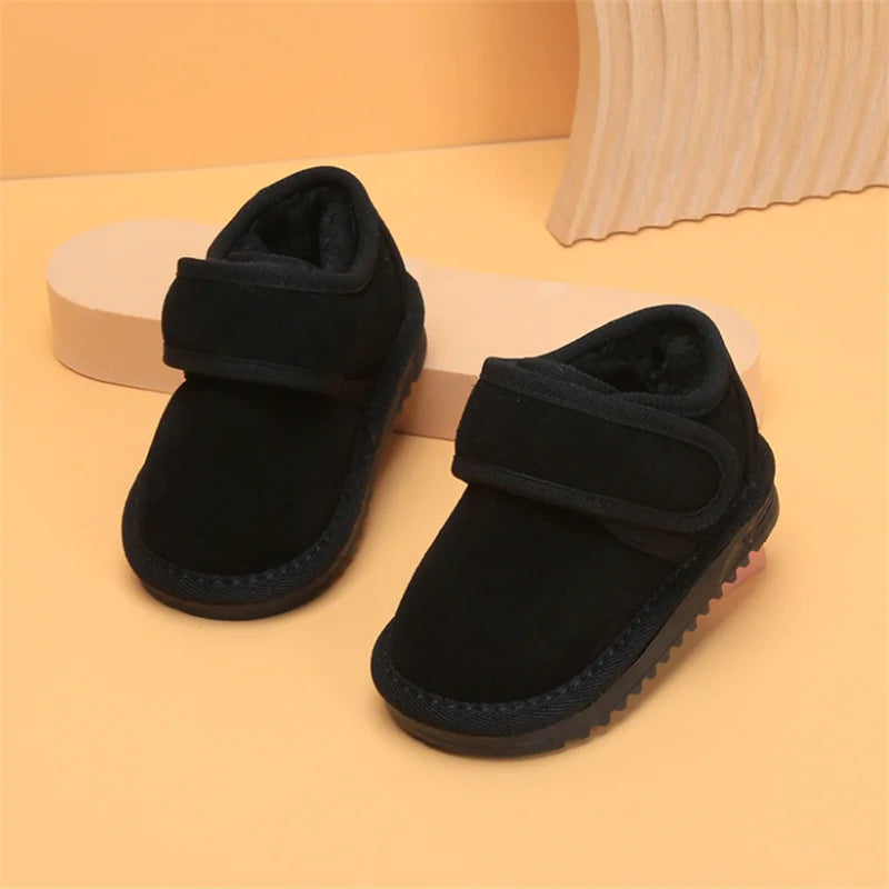 A pair of black cozy leather winter boots for toddlers with anti-slip rubber soles resting on a light orange surface.