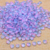 A pile of iridescent purple and pink glass beads scattered on a beige fabric surface.