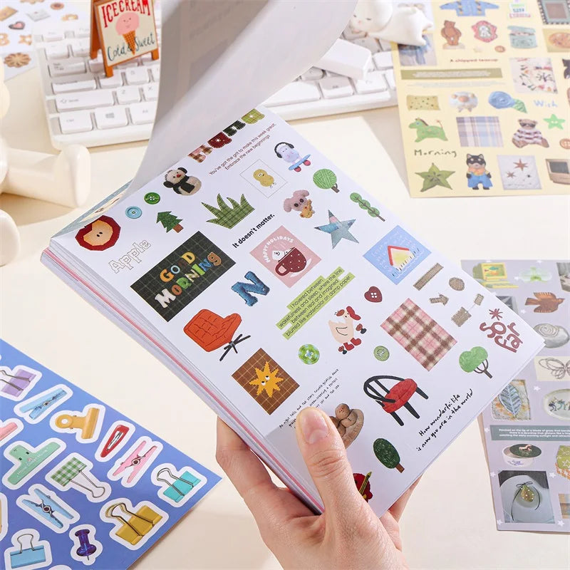 A hand holds an open book filled with retro aesthetic stickers for DIY crafting on a white surface.