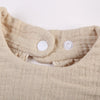 A close-up of a beige ruffled muslin cotton baby bib with an adjustable snap closure.